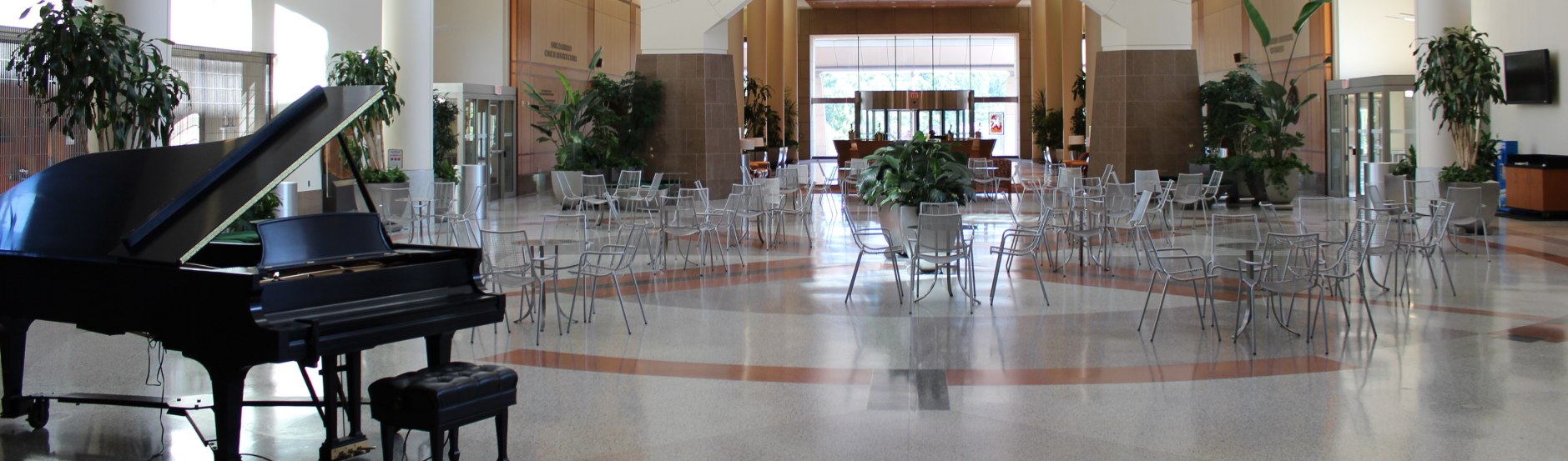 A piano sits in the foreground, while groups of tables and chairs sit in a large room in the background.