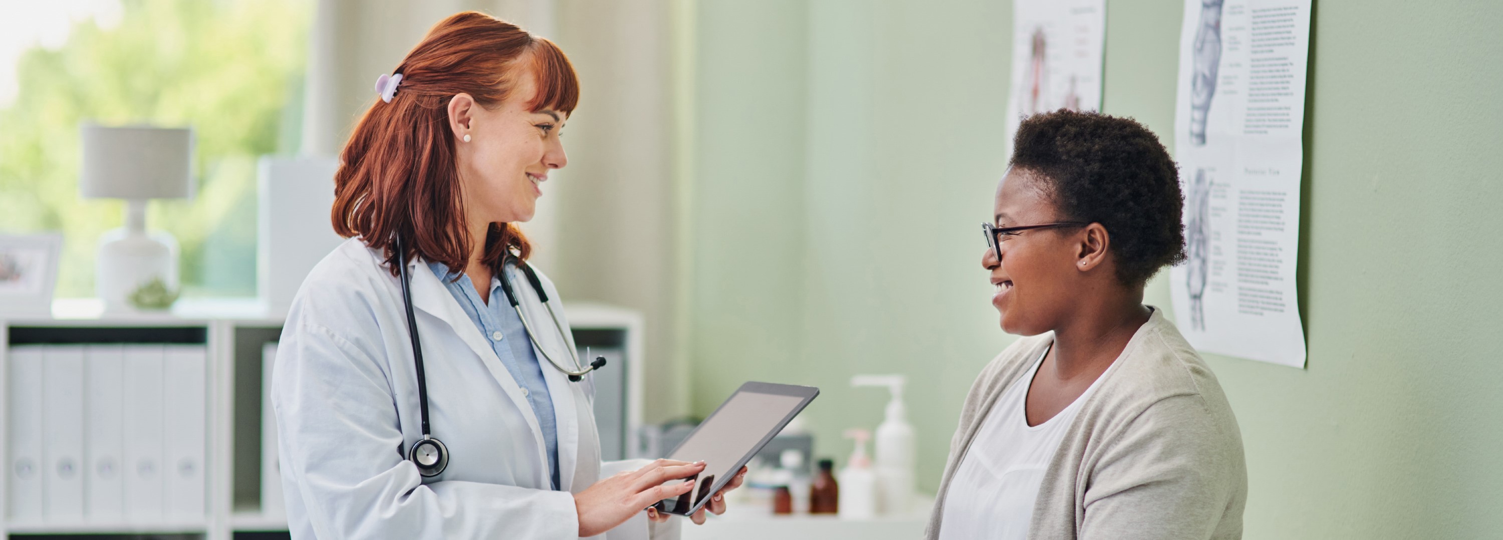 A physician discusses something with a woman while holding a tablet.