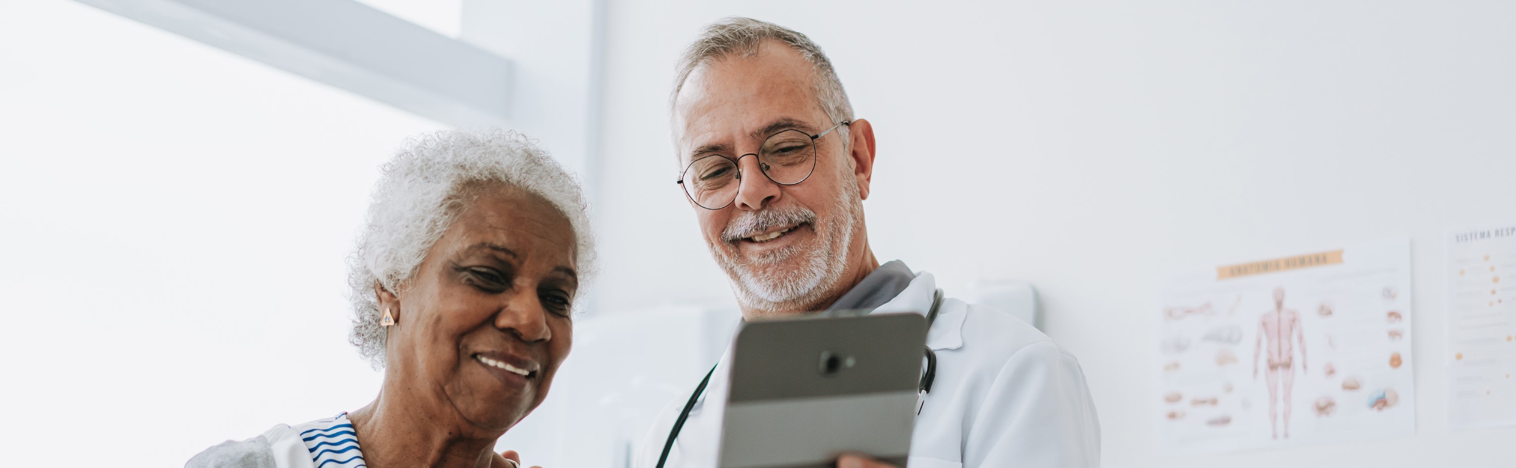 A doctor showing an elderly woman something on a tablet, both smiling.