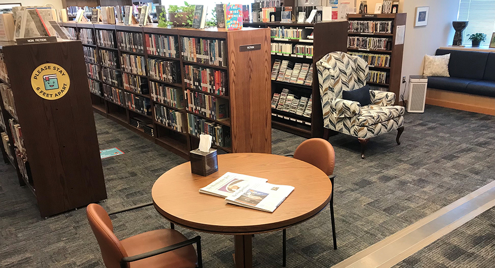 A table with an open book with rows of bookshelves in the background.