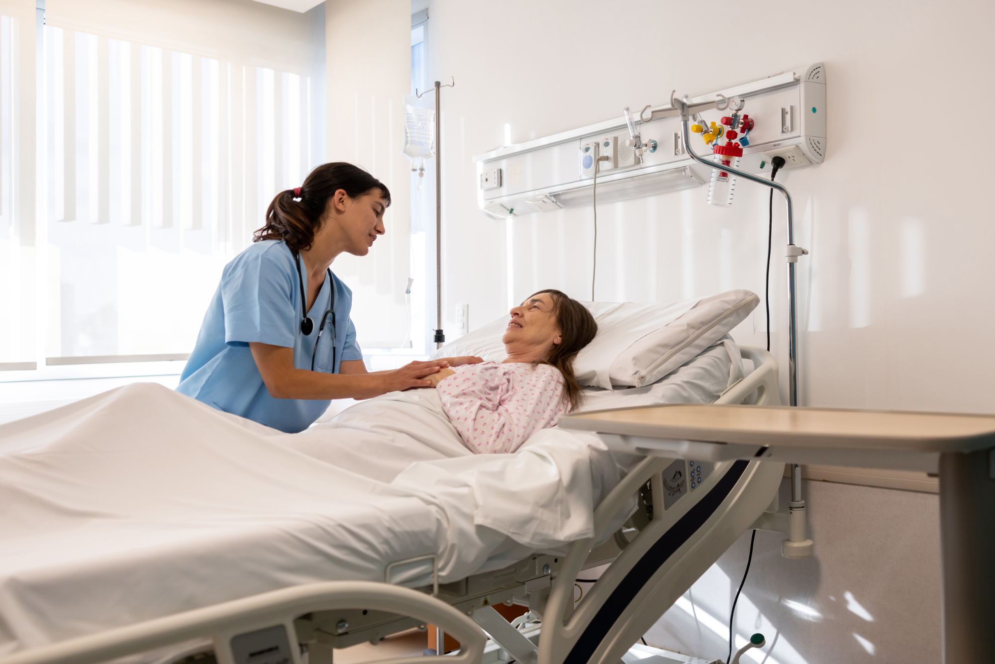 A nurse caring for an elderly patient lying in a hospital bed.