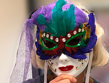 woman holding a Mardi Gras mask to her face