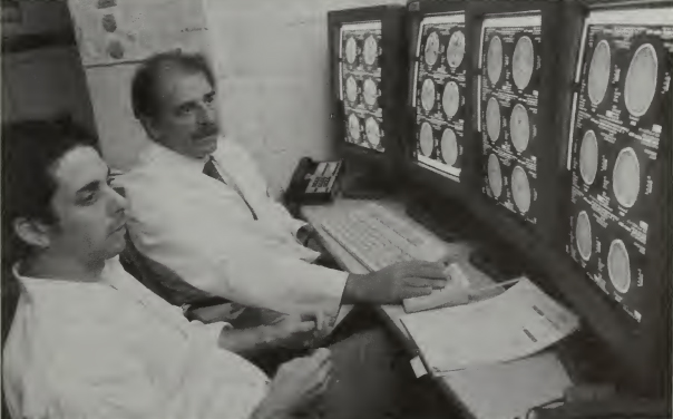 two doctors look at brain scans on large, high-resolution monitors