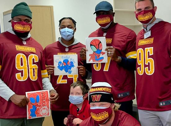 five Washington Commanders  pose with a pediatric patient