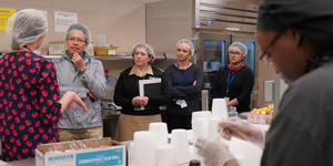 Four people listen to a dietician speak about the Nutrition Department while a employee preps food