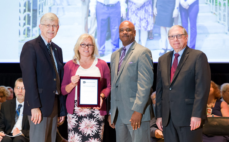 An Optimize NIH IC POC Team representative accepts an award on stage on behalf of the team