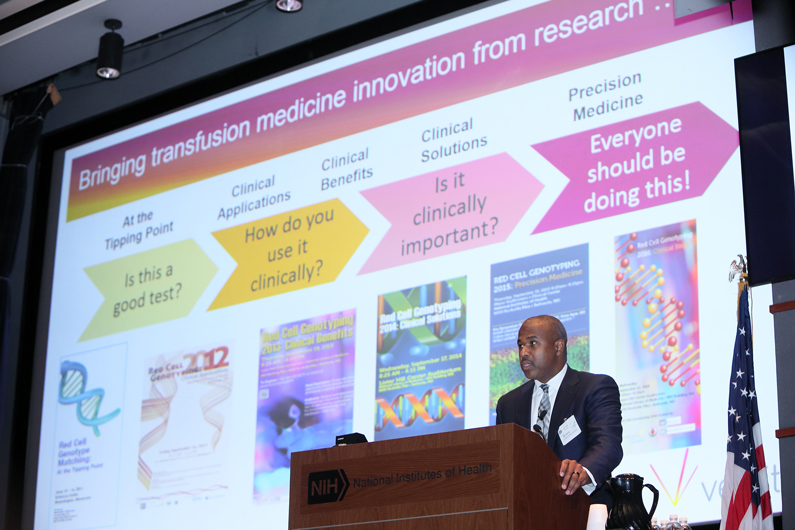 Chris Miskel stands at a podium with a screen behind him that discusses a timeline of bringing transfusion medicine innovation from research to application