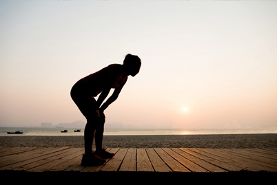 Picture of person winded, bending over, with ocean in the background