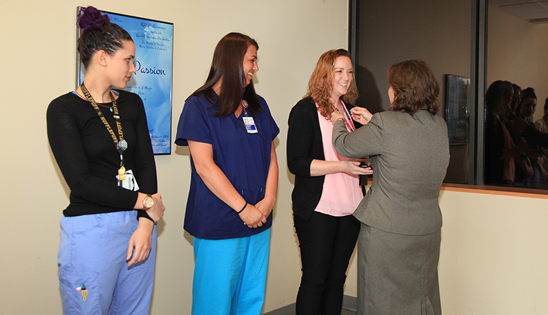 Three young nurses, in scrubs, stand in a line as another woman places a pin on their shirt