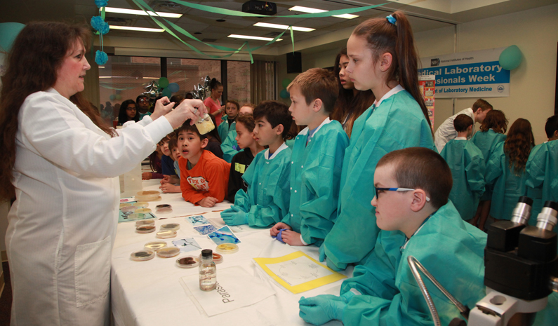 A laboratory technician holds up a bottom of an infectious disease as eight children look on