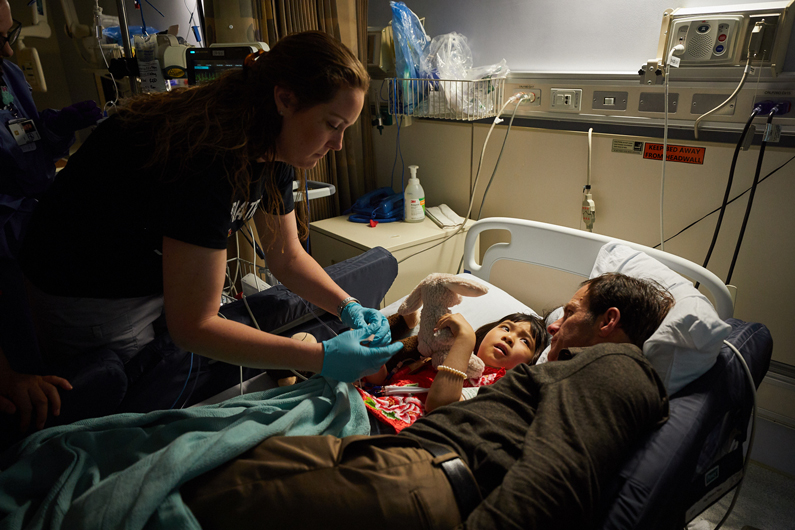 Pediatric patient lays in bed as a nurse situates an IV