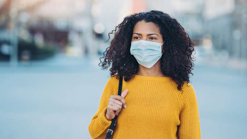 A woman wearing mask walking down sidewalk.