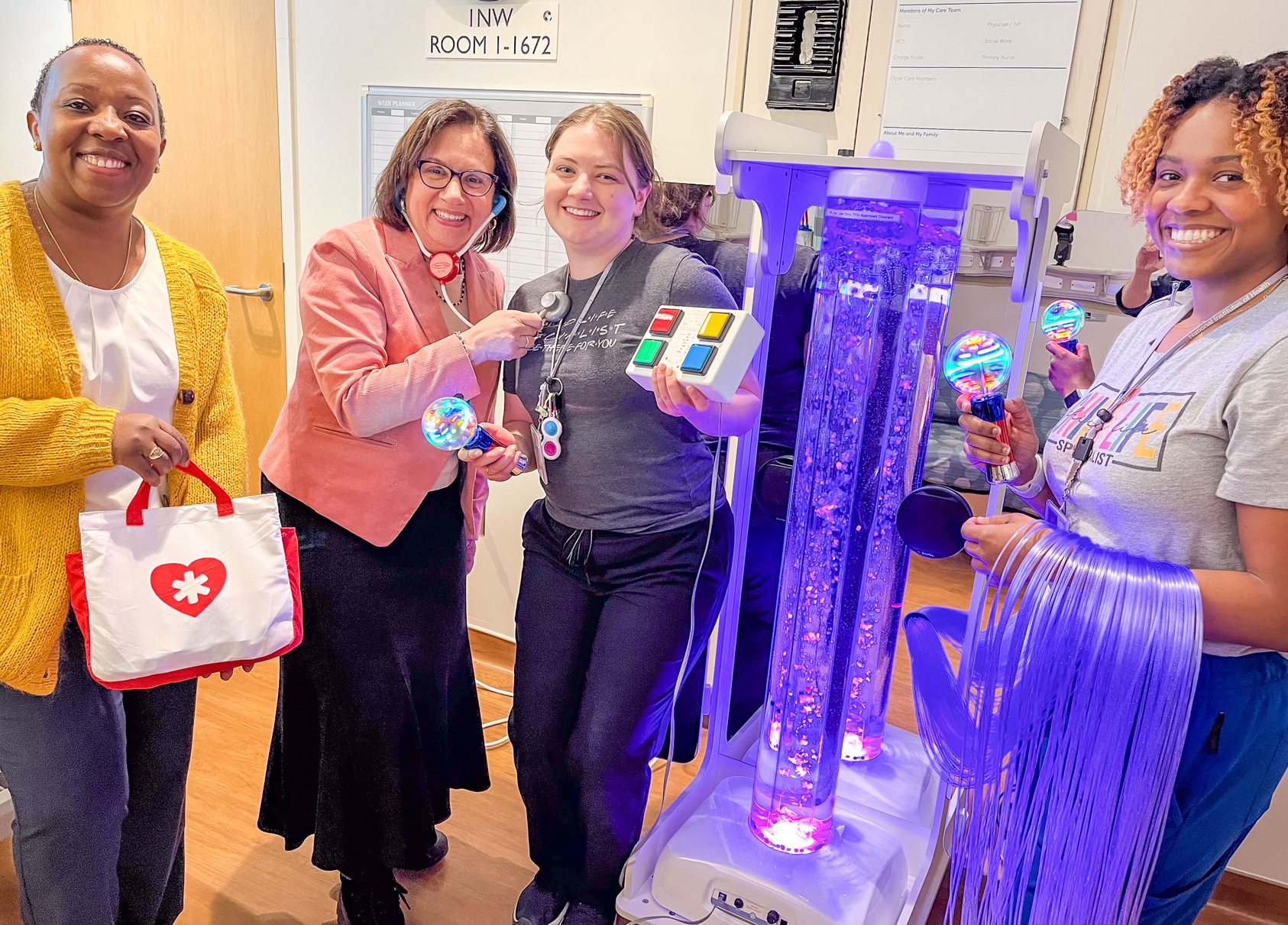 Four medical staff members pose with toys and pediatric medical equipment