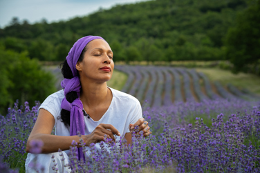 A woman smelling fresh lavender in a sunlit field, with rows of flowers stretching toward the horizon