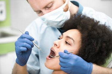 A dentist in blue gloves examining a female patient's teeth in a dental chair
