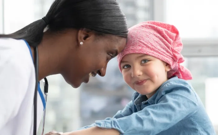 A healthcare professional gently touching foreheads with a smiling young girl wearing a pink headscarf.