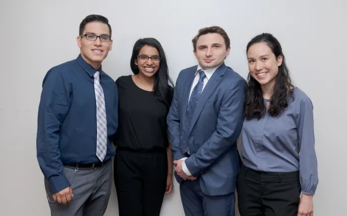 Four professionals, two men and two women, standing together and smiling in business attire.