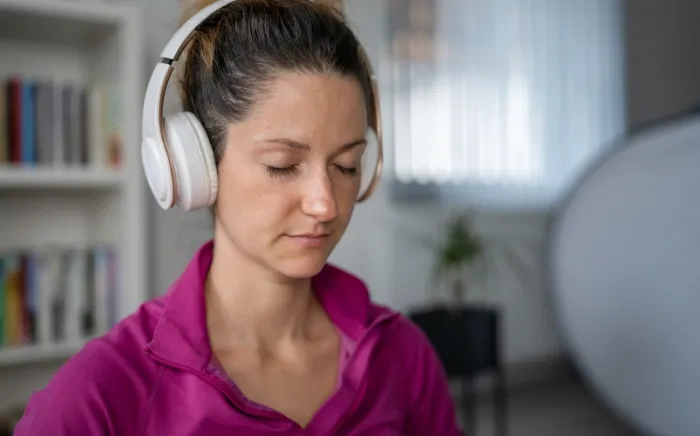 A woman wearing headphones, with her eyes closed, appearing relaxed.