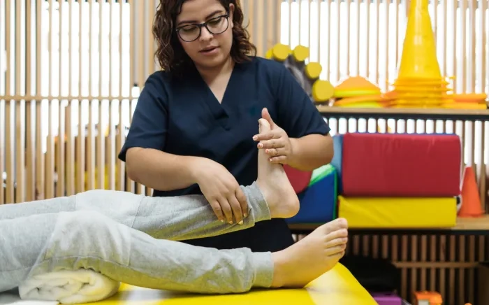 Physical therapist adjusting the ankle of a patient lying on a treatment table in a colorful therapy room.