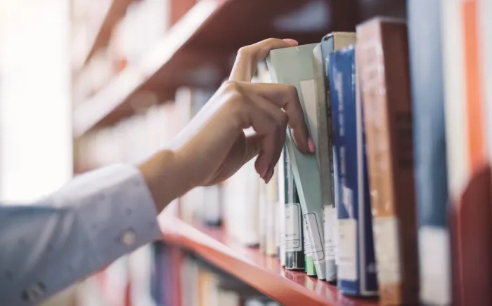 An outstretched hand pulls a book from a bookshelf.