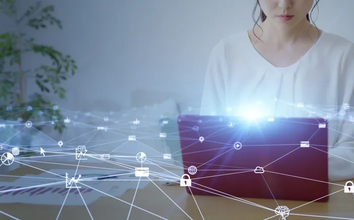 Woman working on a laptop with a digital network overlay depicting interconnected data points and technology icons.