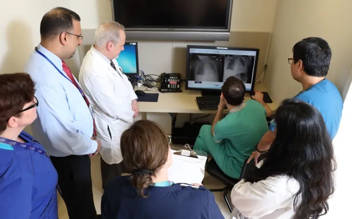 A group of healthcare professionals reviewing X-ray images on a computer screen in a medical office.