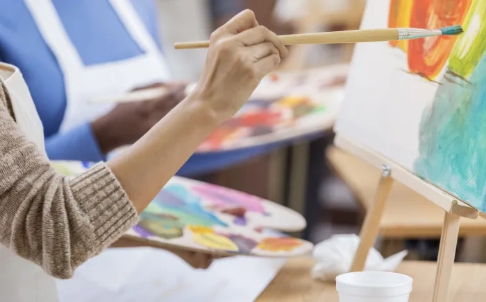 An artist uses a paintbrush to add vibrant colors to a canvas during a painting session, with a palette of mixed paints in the other hand.