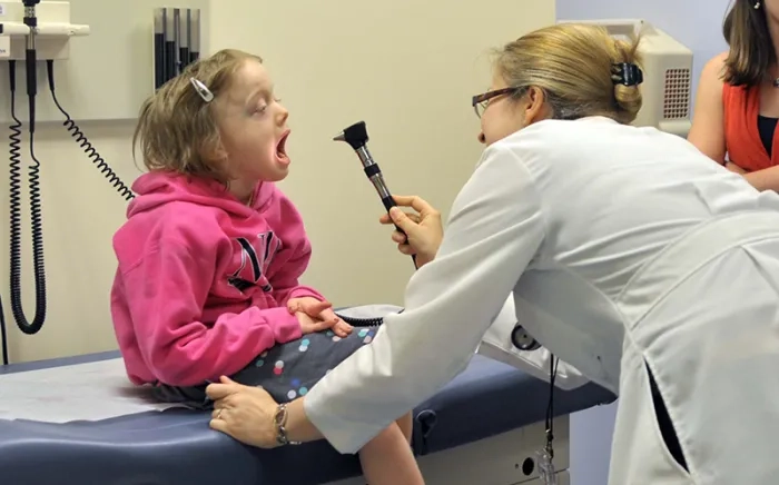 A clinician uses an otoscope to look at a child's throat.