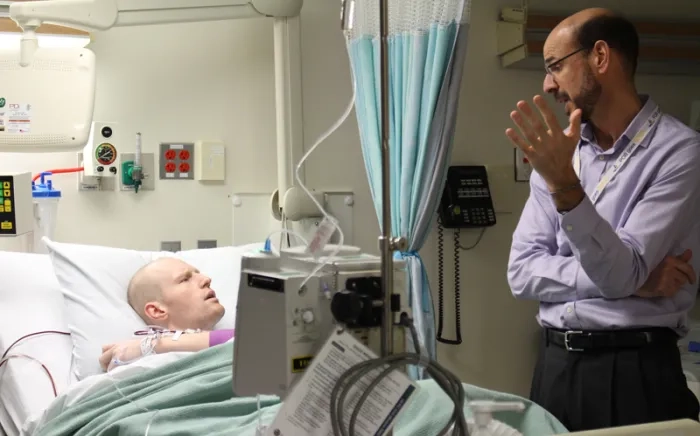 A physician has a discussion with a patient laying in a hospital bed.